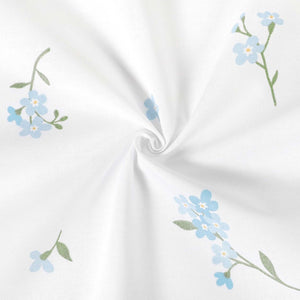 Forget-me-not cotton fabric arranged in a loose swirl, showing blue floral sprigs on white and the fabric’s soft drape