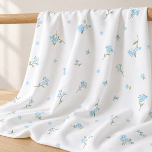 Forget-me-not blue floral cotton fabric draped over an oak rail, showing the scattered flower print and soft folds. Fabric shop UK