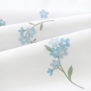 Close-up of Forget-me-not blue floral cotton fabric in soft folds, showing the fine weave, blue petals and muted green stems