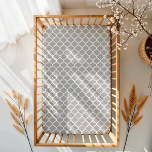 Wooden crib with a gray patterned sheet against a white wall with decorative elements.