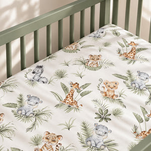 Jungle Animals fitted sheet in a sage green Nestig-style mini crib, beside a light oak table on a natural woven rug.