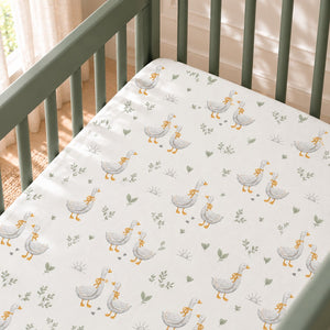 Close-up of the Little Goose fitted sheet in a sage green mini crib, showing grey geese with mustard bows, sage leaves and small footprints on white cotton.