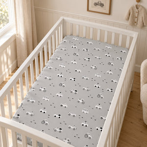 Light grey baby cot fitted sheet with white and black cars, tractors and buses, shown in a white cot in a neutral nursery.