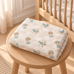 Folded Safari Pilots cotton baby fitted sheet with beige and mint animal and aeroplane print on an oak stool