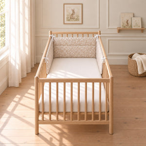 Beige meadow flower bumper across the head and halfway down both sides of a light oak cot, with white ties in a neutral nursery.