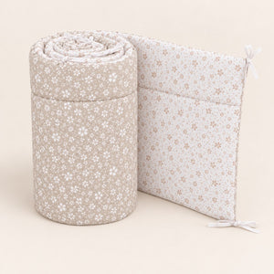 Upright rolled meadow floral cot bumper showing white flowers on light beige, beige flowers on the white reverse, quilting and white ties.