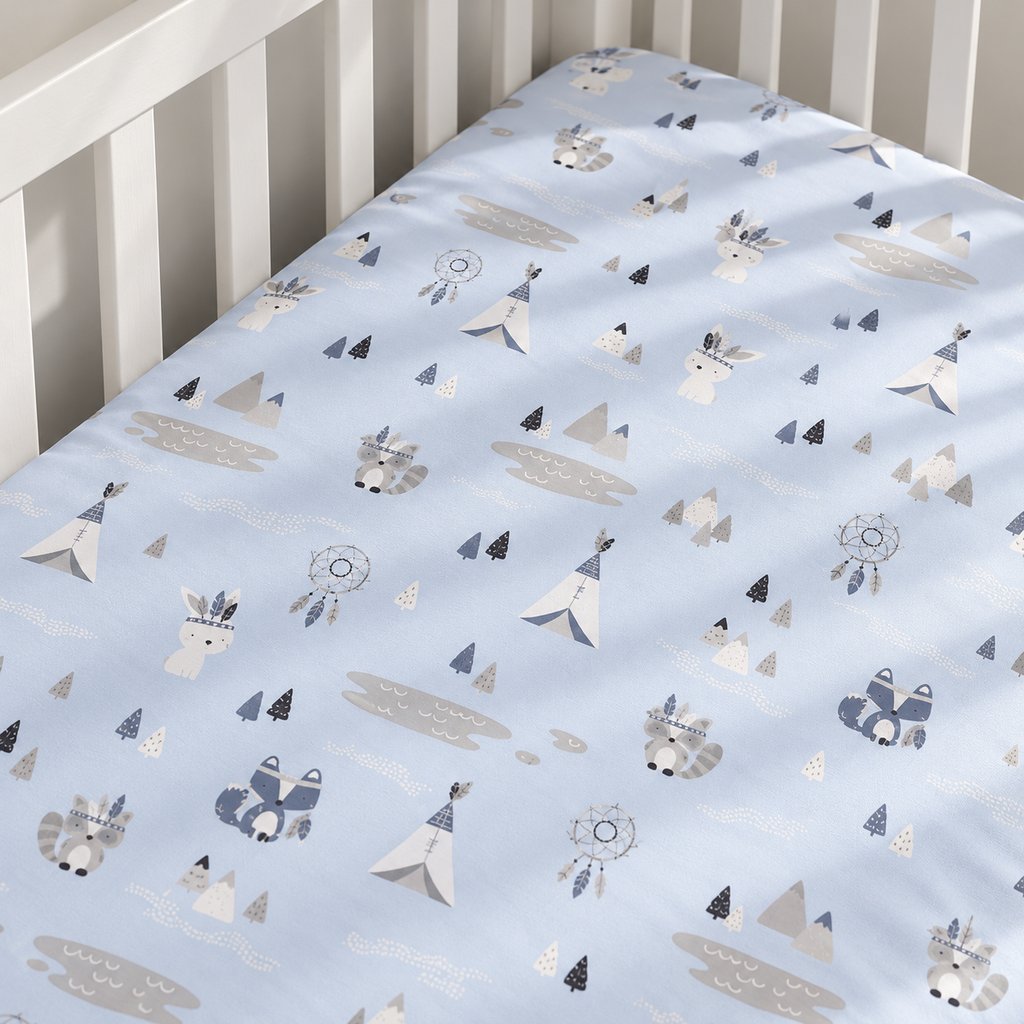 Close-up of pale blue cotton baby fitted sheet with foxes, rabbits, raccoons, teepees and dreamcatchers in a white cot