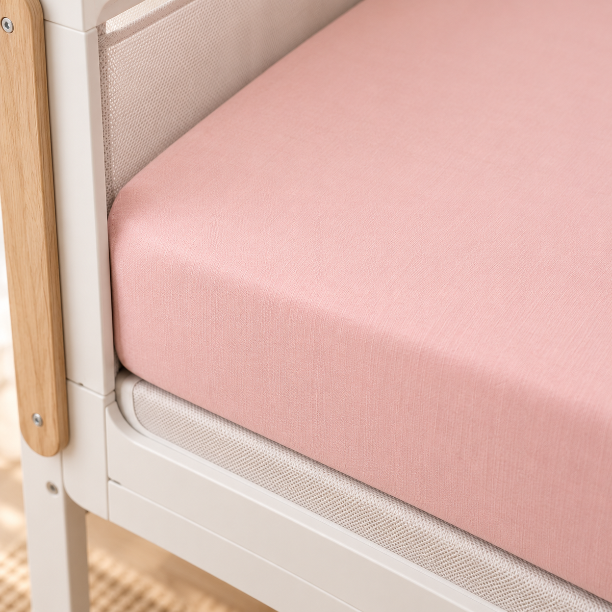 Close-up of a blush pink SnuzPod fitted sheet showing its smooth elasticated fit and cotton texture