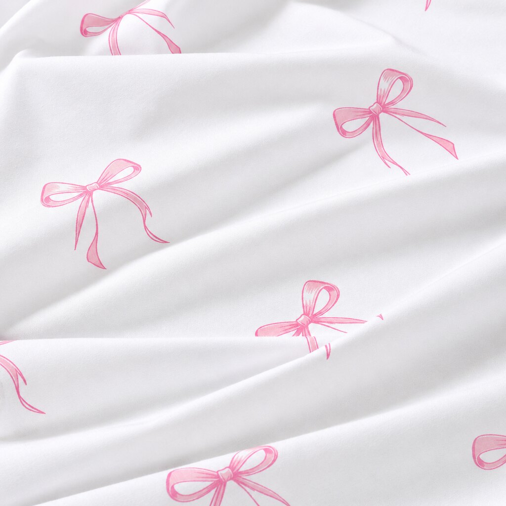 Close-up of white OEKO-TEX® 100% cotton fabric with pink coquette ribbon bows, sold by the metre in the UK.