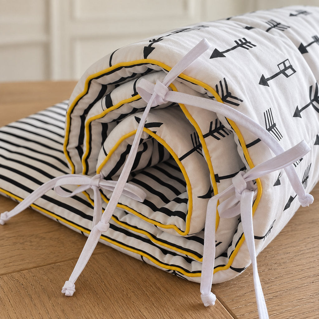 Detail of black arrow cot bed bumper with striped cotton reverse and  yellow piping