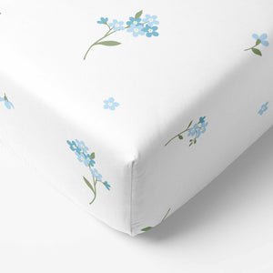 Close-up of the fitted corner and blue forget-me-not print on a white baby cot sheet