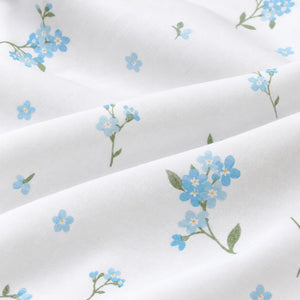 Close-up of Forget-me-not cotton fabric showing pale blue flowers, muted green leaves and fine cotton weave on white