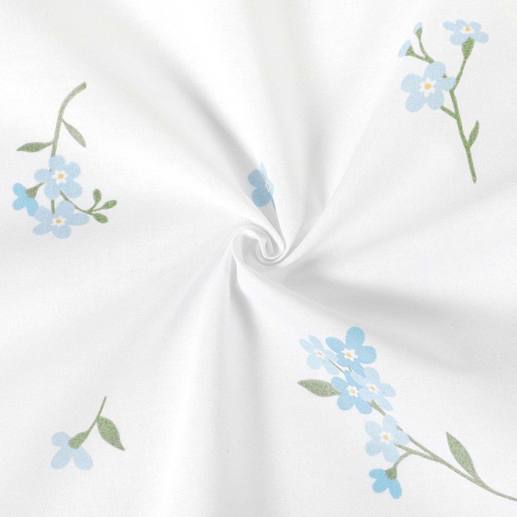 Forget-me-not cotton fabric arranged in a loose swirl, showing blue floral sprigs on white and the fabric’s soft drape
