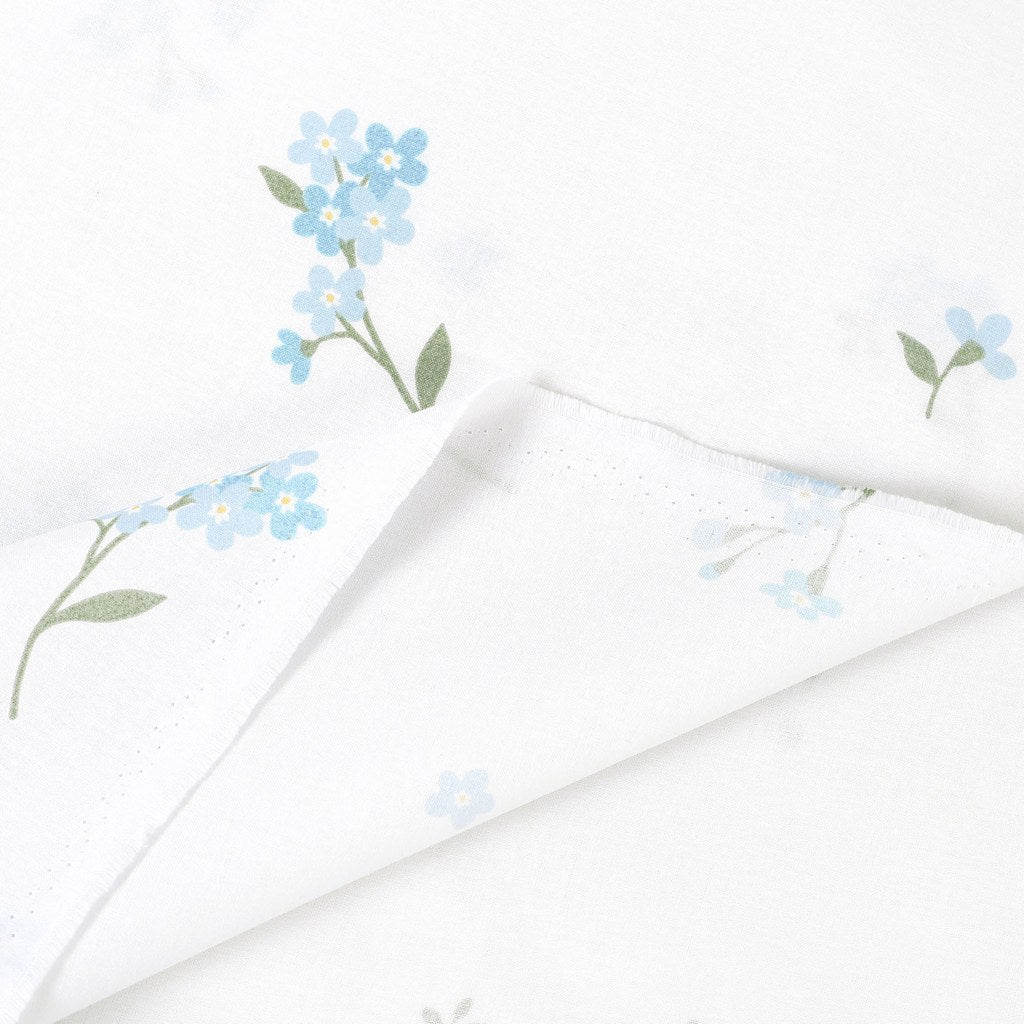 Forget-me-not cotton fabric showing the selvedge and folded reverse, with pale blue flowers and green leaves on white