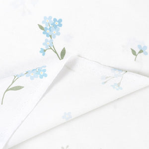 Forget-me-not cotton fabric showing the selvedge and folded reverse, with pale blue flowers and green leaves on white