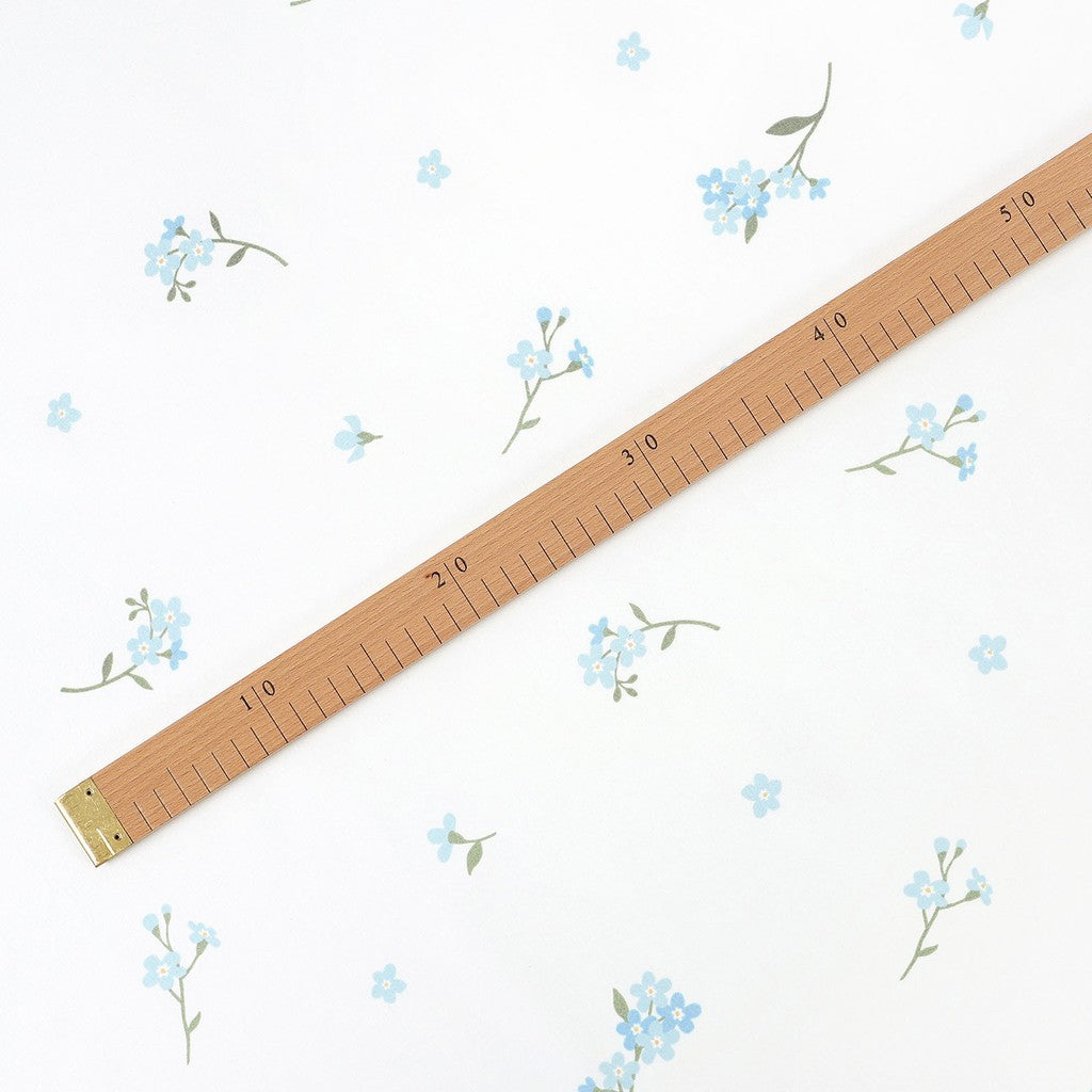 Forget-me-not blue floral cotton fabric beside a wooden centimetre ruler, showing flower size and pattern spacing