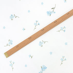Forget-me-not blue floral cotton fabric beside a wooden centimetre ruler, showing flower size and pattern spacing
