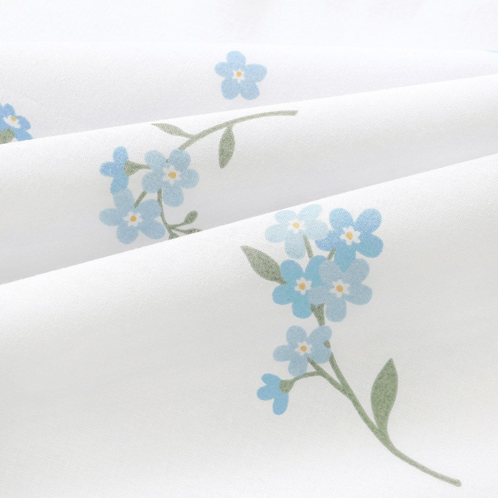 Close-up of Forget-me-not blue floral cotton fabric in soft folds, showing the fine weave, blue petals and muted green stems