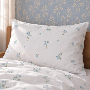 Close-up of the matching Forget Me Not floral pillowcase on an oak bed against a pale blue botanical wall