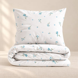 Folded white Forget Me Not duvet cover with matching floral pillowcase against a soft ivory background