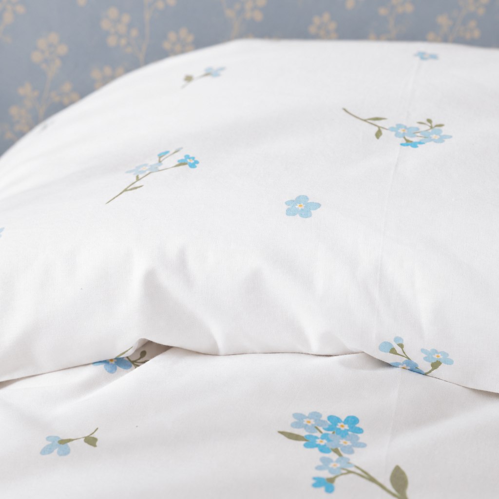 Close-up of the matching Forget Me Not floral pillowcase on an oak bed against a pale blue botanical wall