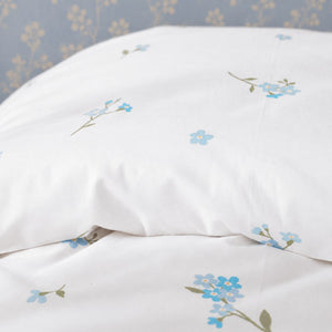 Close-up of the matching Forget Me Not floral pillowcase on an oak bed against a pale blue botanical wall
