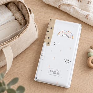 Giraffe and koala travel changing mat folded into a compact rectangle beside a beige changing bag.