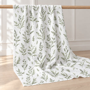 Green botanical print fabric draped over a wooden rail, showing its vertical branches and soft folds
