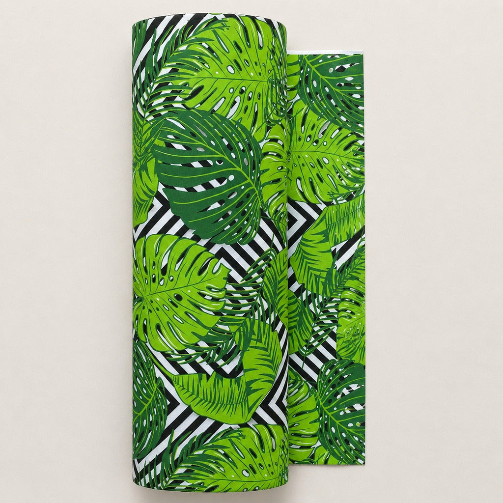 Monstera leaf cotton fabric on a roll from Fabricco UK with green tropical foliage and black and white geometric background.