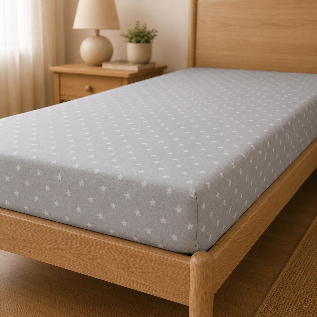 Close up of fully elasticated grey fitted sheet with white stars on single bed