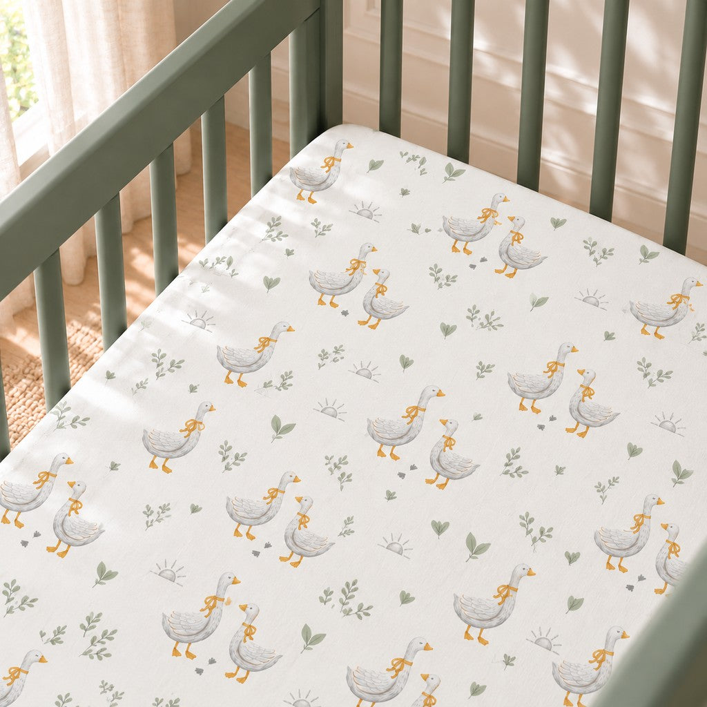 Close-up of the Little Goose fitted sheet in a sage green mini crib, showing grey geese with mustard bows, sage leaves and small footprints on white cotton.