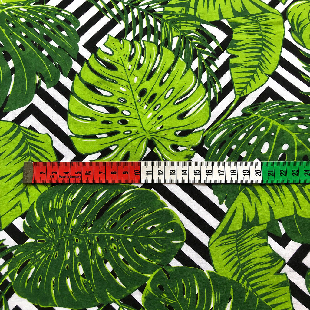 Close-up of green Monstera leaf cotton fabric from Fabricco UK with tropical botanical foliage on a black and white geometric background.