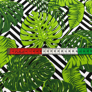 Close-up of green Monstera leaf cotton fabric from Fabricco UK with tropical botanical foliage on a black and white geometric background.
