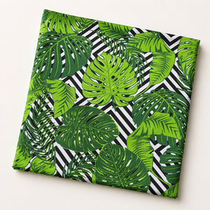 Green Monstera leaf cotton fabric by the metre from Fabricco UK with bold tropical leaves and black and white geometric print.
