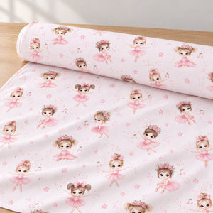 Pink ballerina cotton fabric unrolled on a light oak table, showing little ballet dancers, stars and musical notes