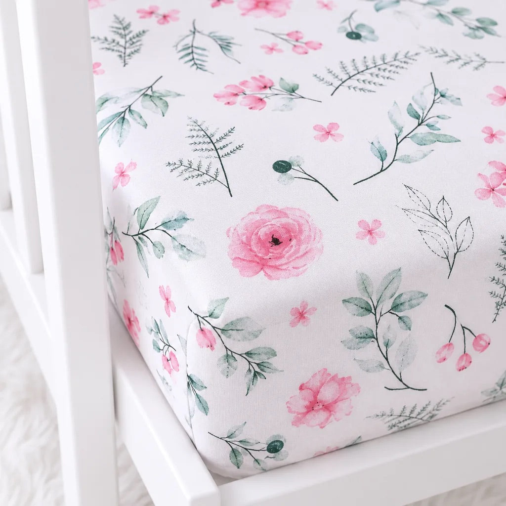 Close-up of pink floral cotton cot fitted sheet showing botanical print and fitted mattress corner