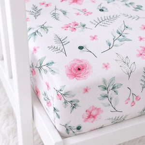 Close-up of pink floral cotton cot fitted sheet showing botanical print and fitted mattress corner