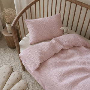 Pink seersucker cot and cot bed bedding set with tiny white flowers styled in a Scandinavian nursery
