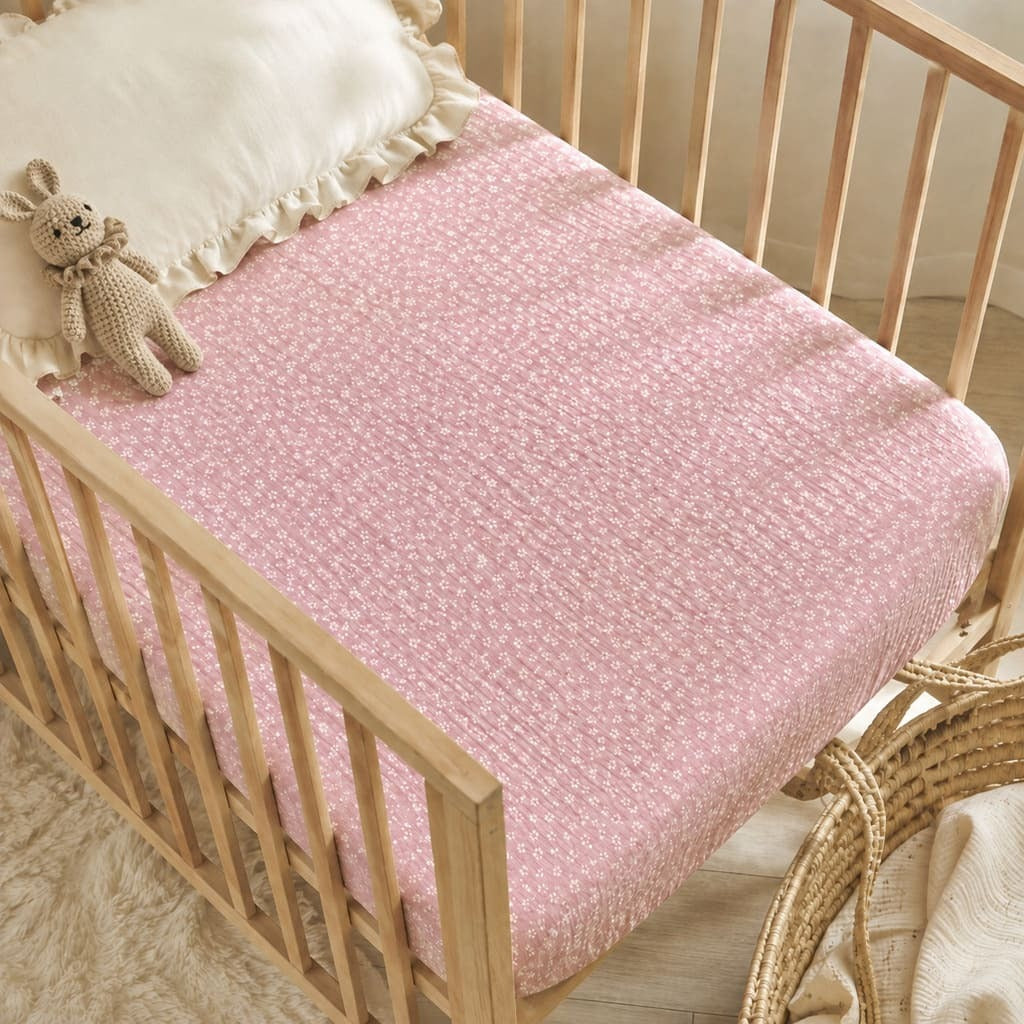 Pink seersucker fitted sheet on a cot mattress styled in a soft Scandinavian nursery