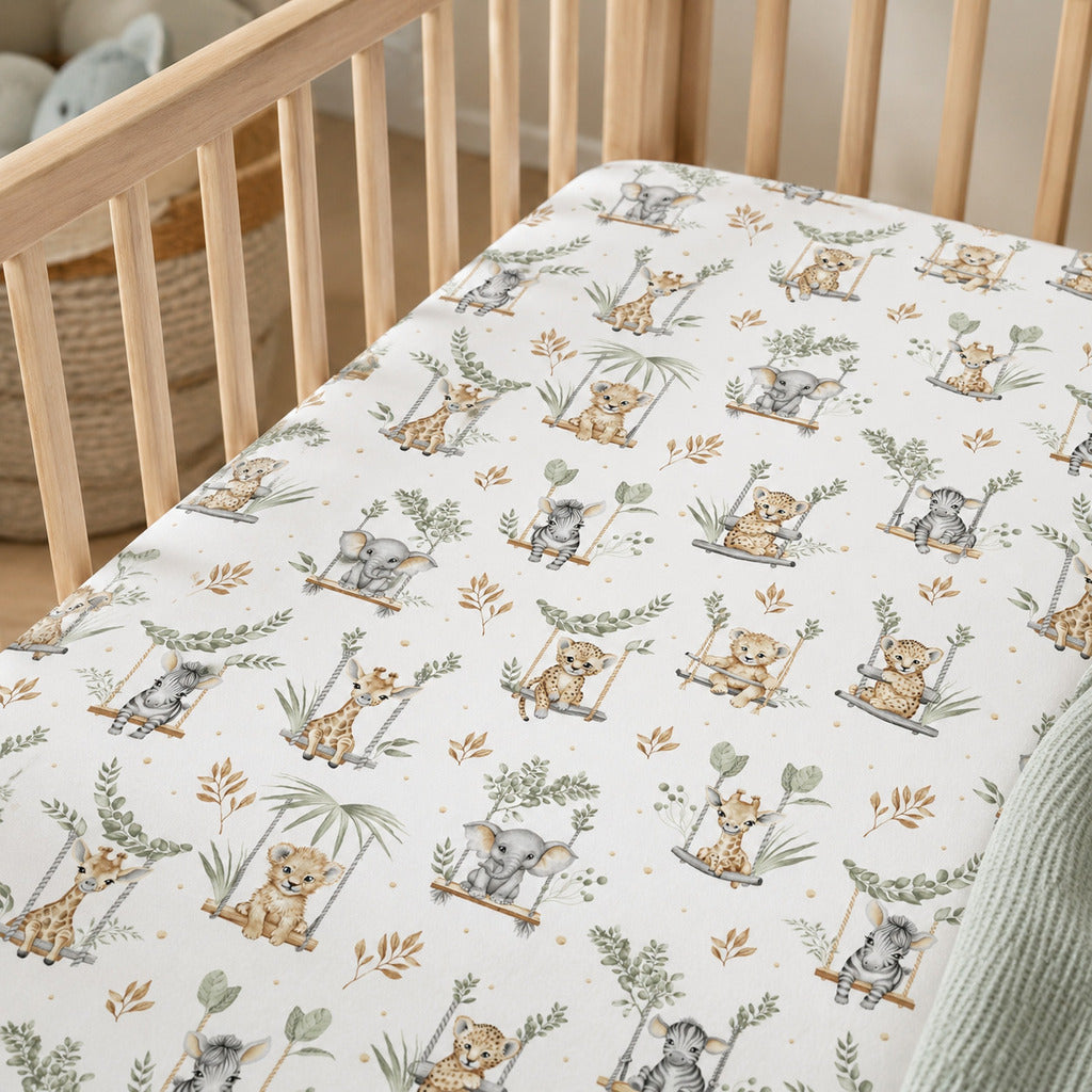 Close-up of sage safari cot fitted sheet showing elephants, giraffes, zebras, lions and leafy details on white cotton