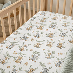 Close-up of sage safari cot fitted sheet showing elephants, giraffes, zebras, lions and leafy details on white cotton