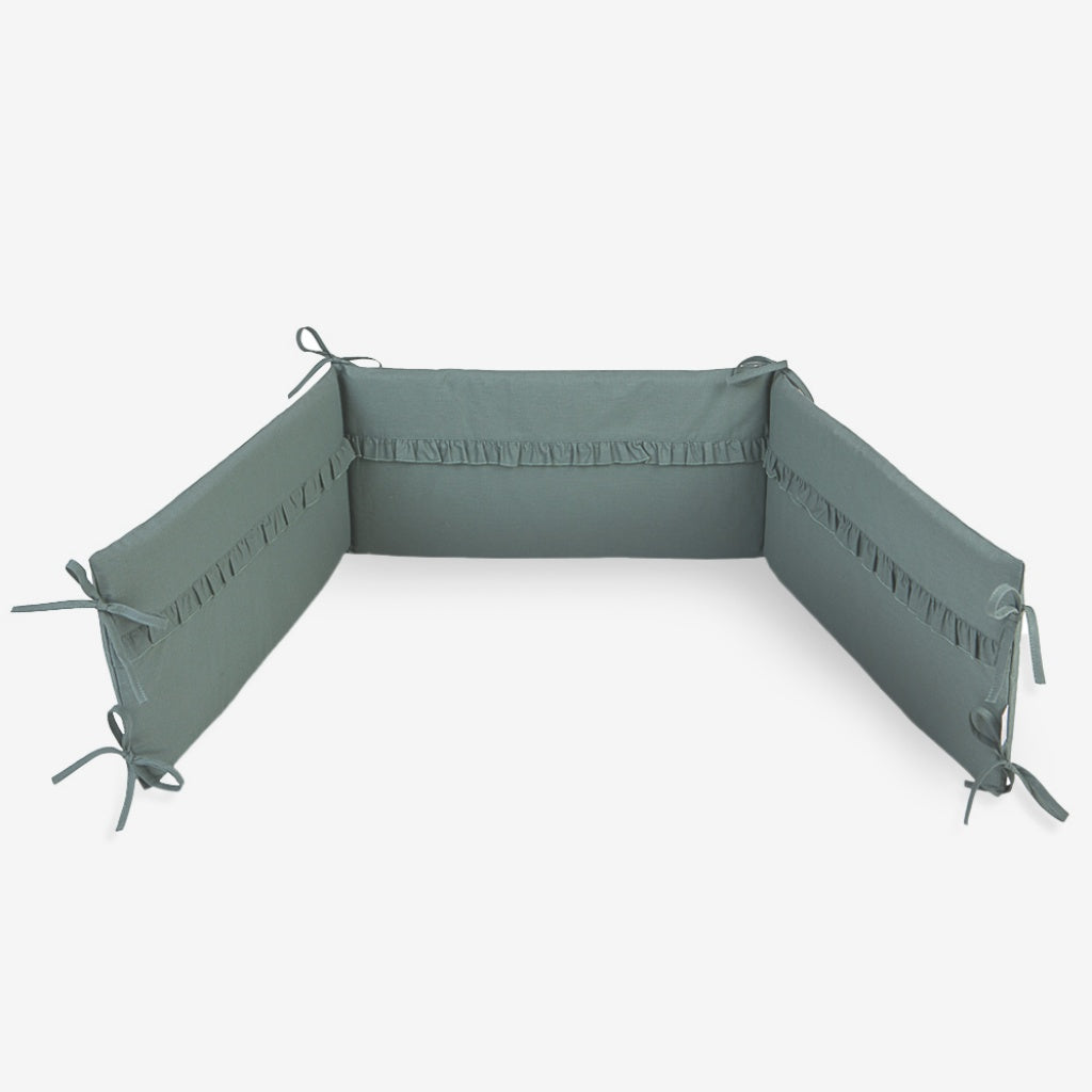 UK Sage green breathable cot bumper secured with fabric ties inside a baby cot, quilted nursery bedding protector for 120x60 cm standard cot size.