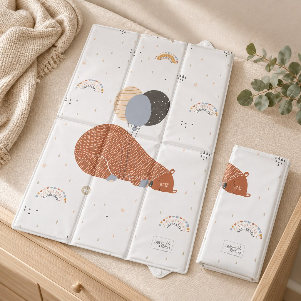 Sleeping bear and balloons travel changing mat shown unfolded and folded on a cream-covered oak dresser beside a knitted throw.