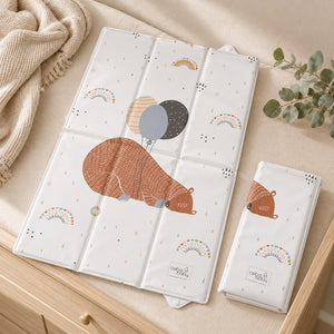 Sleeping bear and balloons travel changing mat shown unfolded and folded on a cream-covered oak dresser beside a knitted throw.