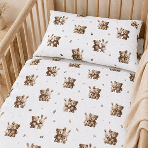 Close-up of teddy bear and bunny cot bedding showing beige and brown characters with delicate leaves on white cotton