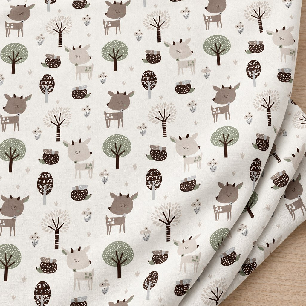 Softly folded white cotton fabric with beige and brown woodland deer, hedgehogs and decorative trees