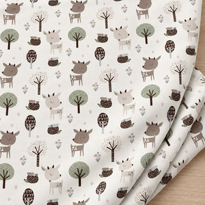 Softly folded white cotton fabric with beige and brown woodland deer, hedgehogs and decorative trees