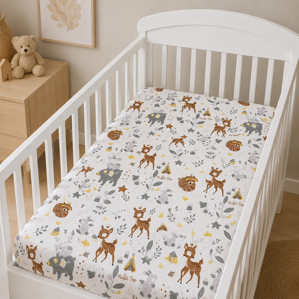 A fitted crib sheet with a woodland animal print is shown on a white wooden toddler bed. The sheet features brown deer, gray elephants, yellow triangles, and small brown bears on a white background