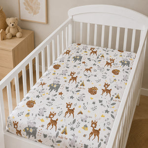 A fitted crib sheet with a woodland animal print is shown on a white wooden toddler bed. The sheet features brown deer, gray elephants, yellow triangles, and small brown bears on a white background
