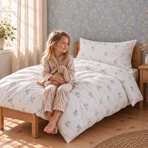 Child sitting on a single bed with Forget Me Not blue floral cotton bedding set, handmade in the UK by Fabricco